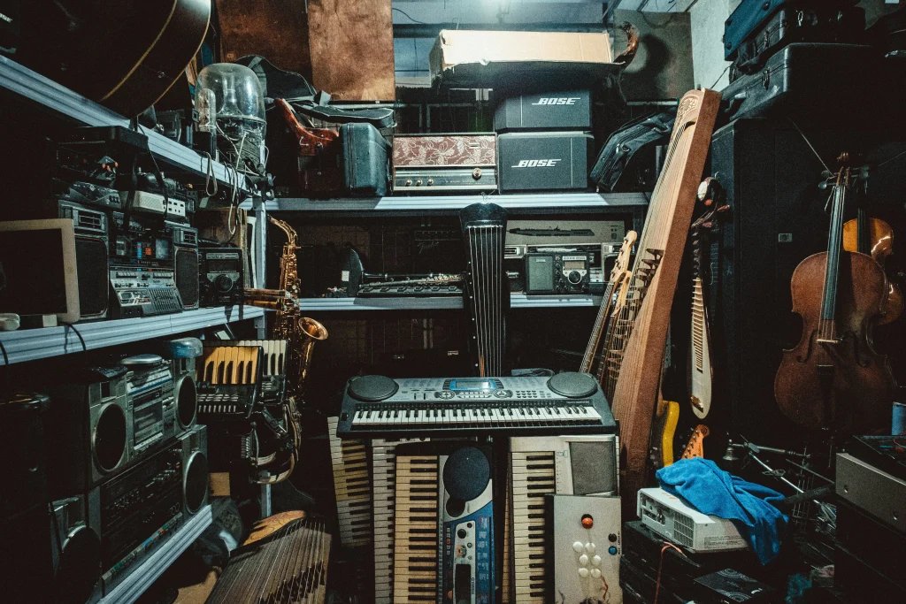 Ett överfullt förråd fyllt med mängder av musikinstrument och äldre elektronik. I mitten syns flera staplade keyboardar omgivna av metallhyllor fyllda med retro bergsprängare, stereoutrustning, högtalarlådor (bland annat från Bose), ett dragspel och en saxofon. Till höger syns olika stränginstrument, däribland gitarrer, en cello samt traditionella asiatiska stränginstrument som en pipa och en guzheng.